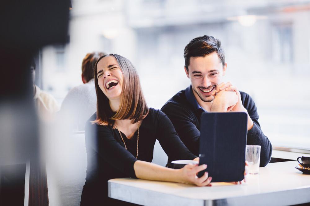 man and woman laughing at work while looking at a tablet