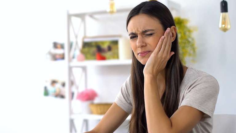 woman holding her left face indicating a potential dental emergency