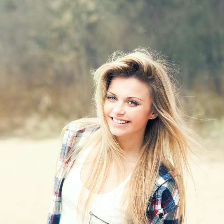 woman in plaid shirt smiling outside | dental crowns mesquite tx